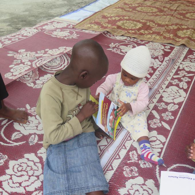 A little girl helps out a baby with a book